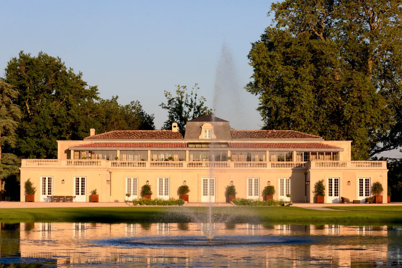 A grand Bordeaux château reflected in a still pond at golden hour